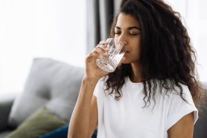 Woman wearing a white shirt, enjoying a glass of fresh water in her home 